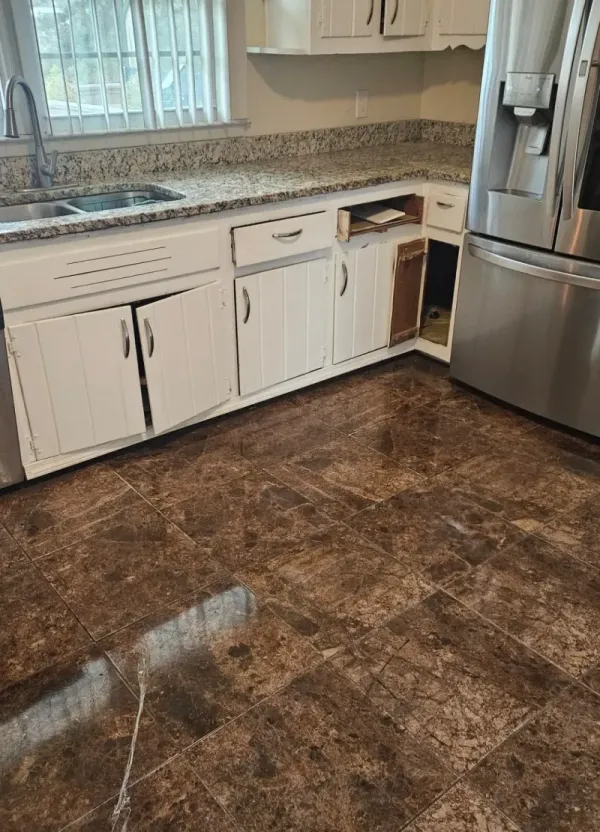 Worn kitchen with broken cabinet door taped shut, dated beige granite countertop, and glossy terracotta tile flooring.