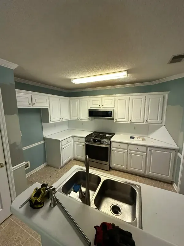 Kitchen during construction, walls stripped to drywall and floor stripped to subfloor, with utilities exposed.